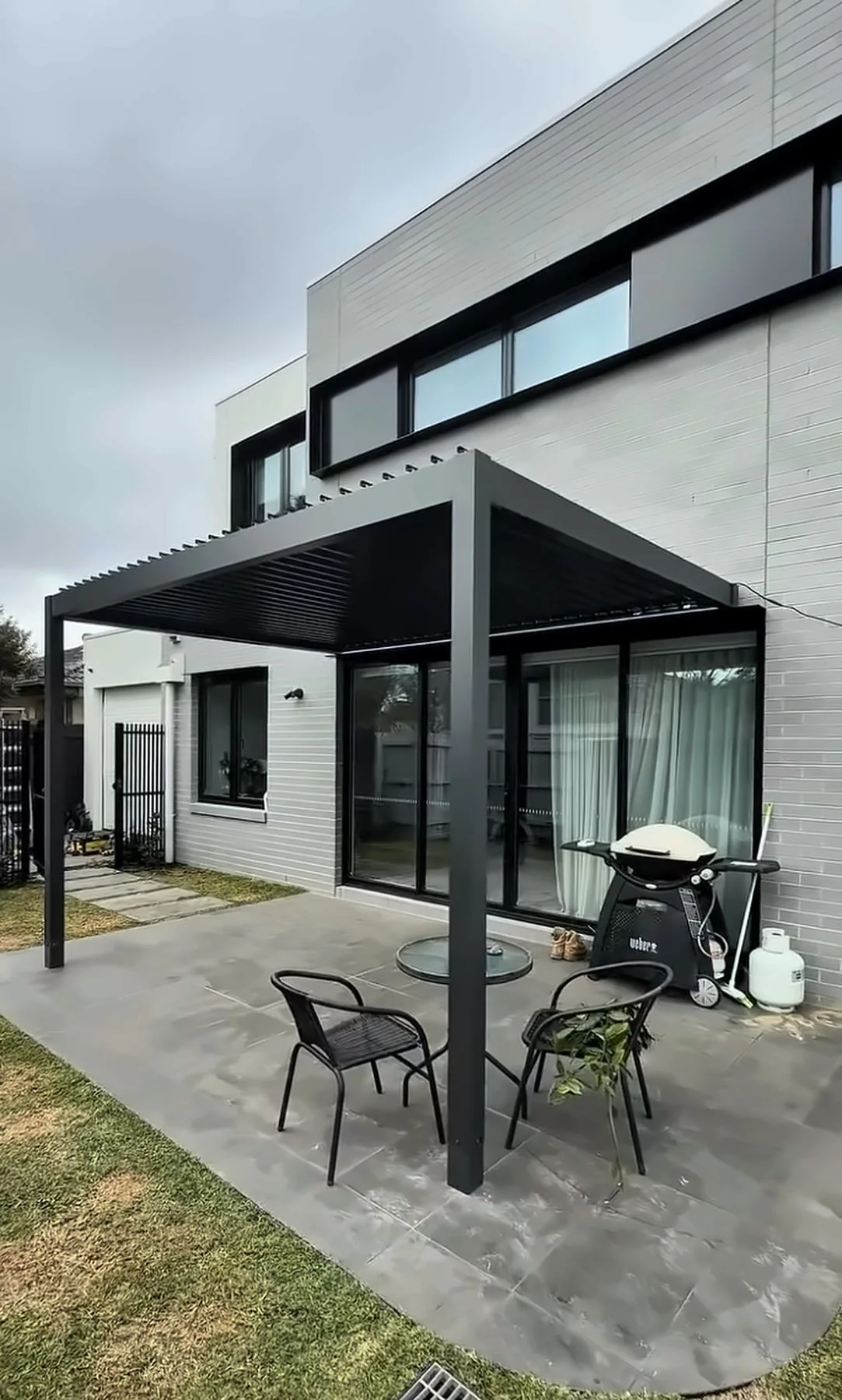 Black louvered pergola over a paved patio